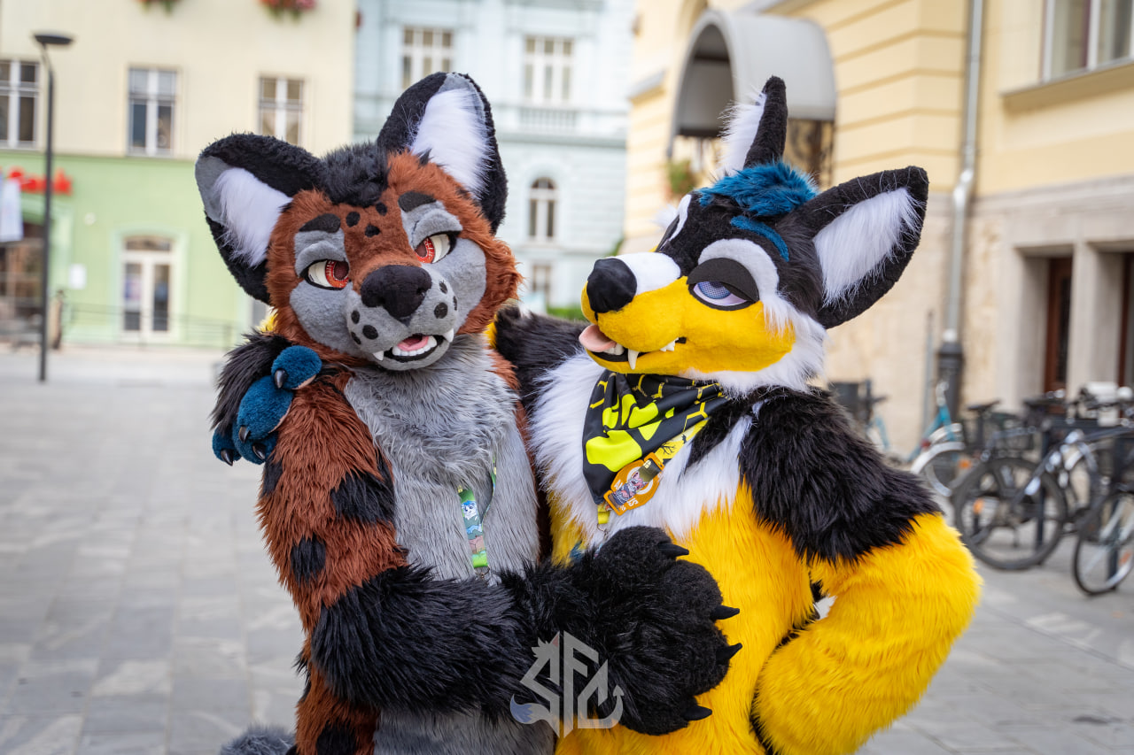 Two fursuiters posing on a cobblestone street at the SloFluffCon furwalk