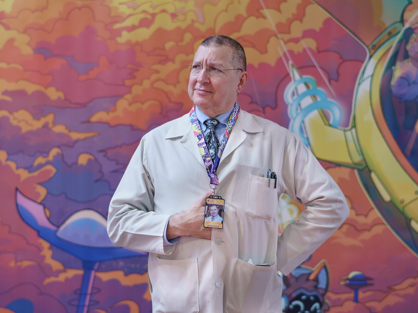 Uncle Kage in his white lab coat, standing in front of a colourful convention mural
