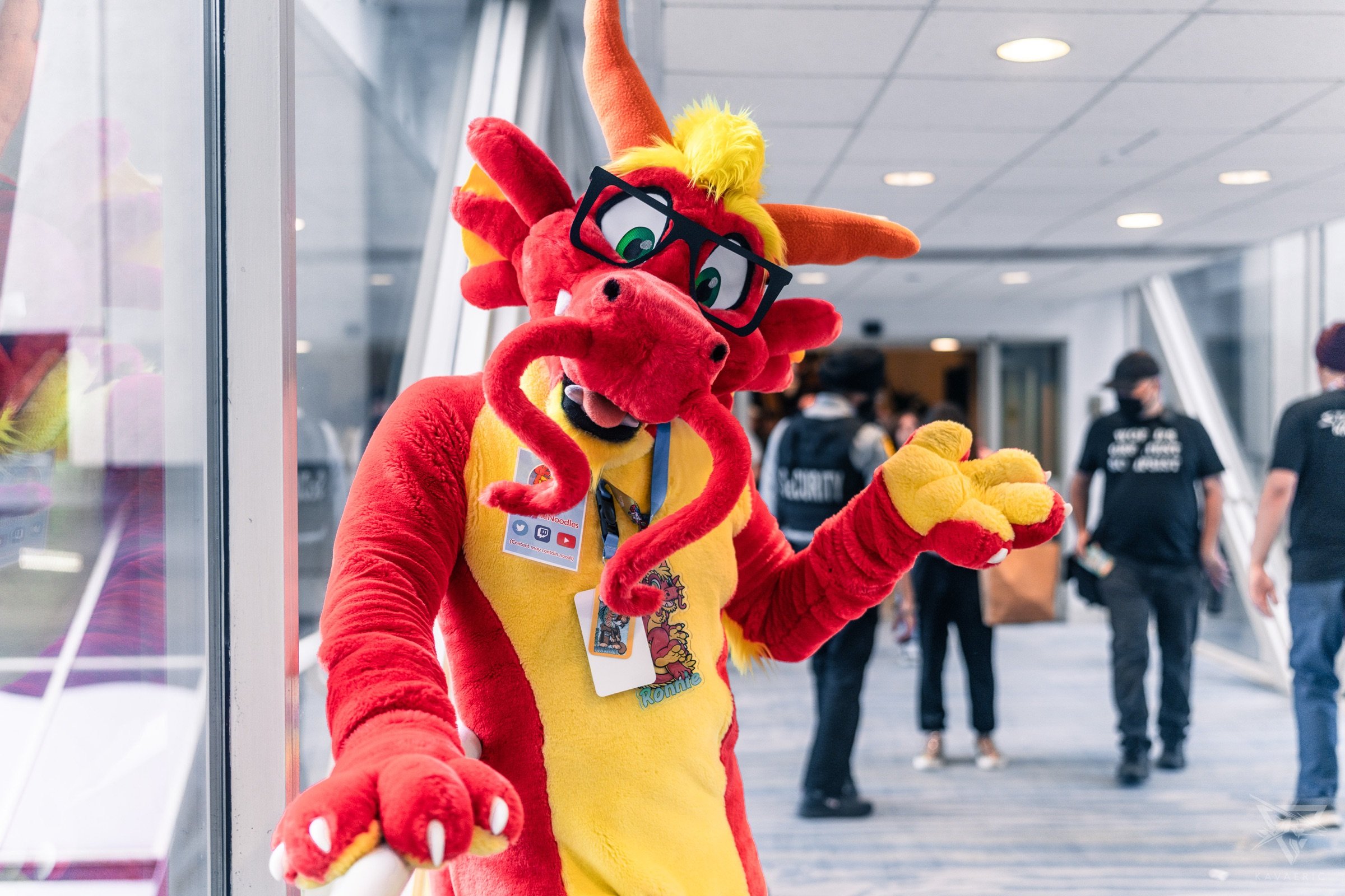 Ronnie Noodles wearing glasses and a badge, waving in a convention skywalk